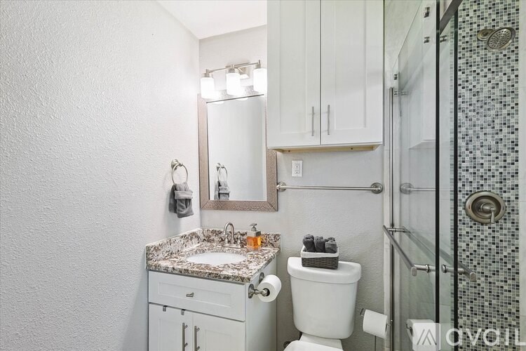 A white bathroom with a marble counter top and a glass shower stall.