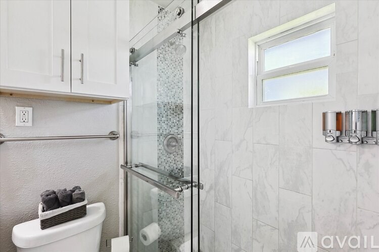 A bathroom with a glass shower door and a toilet with a tissue roll on top.