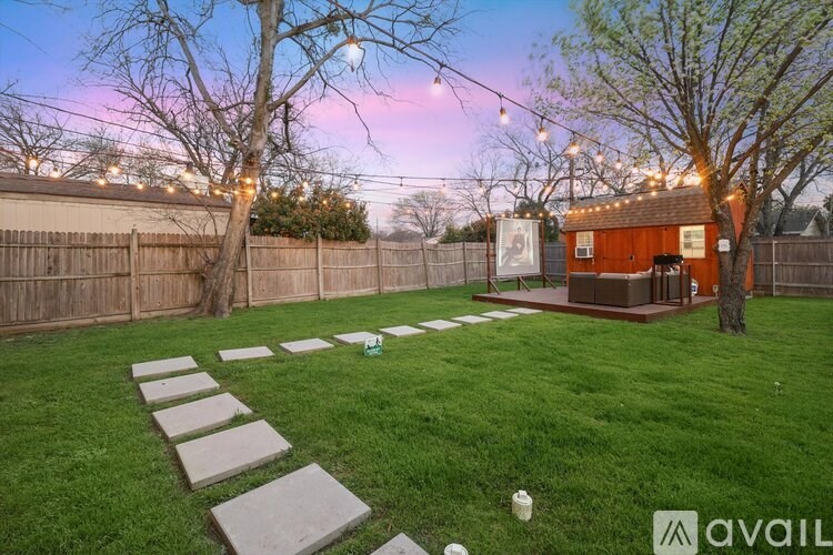 A backyard with a lawn, stepping stones, and a small building.