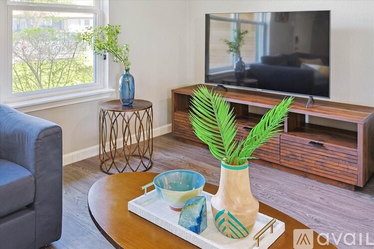 A living room with a grey sofa, a wooden coffee table with a plant and vases on it, and a television on a stand.