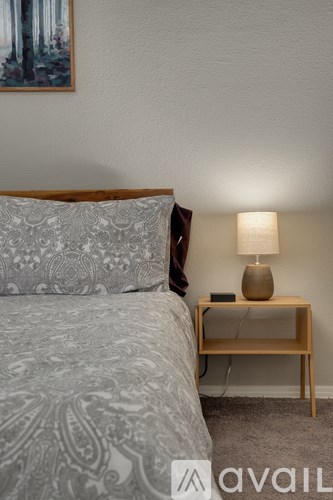 A bedroom with a bed, a nightstand with a lamp, and a painting on the wall.