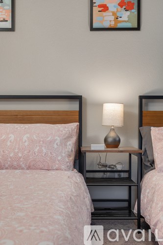 Two beds with pink bedspreads and a nightstand with a lamp between them.