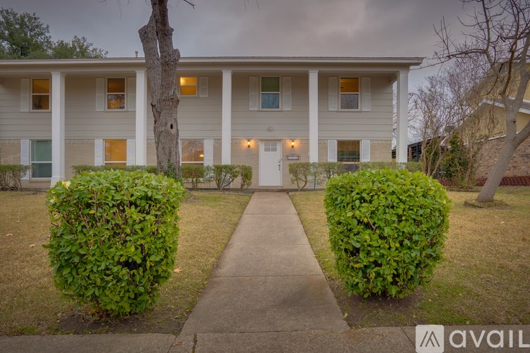 A building with a white door and windows is surrounded by green bushes.