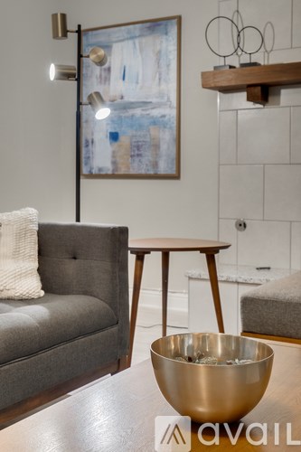 A grey couch with a white pillow sits in a living room with a wooden table and a bowl on it.