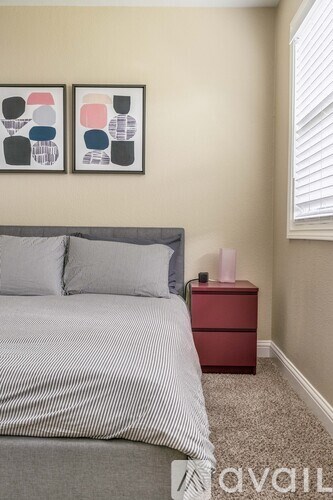 A bedroom with a bed, nightstand, and two abstract paintings on the wall.