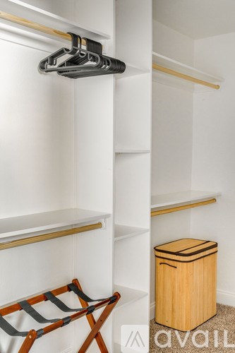 A wooden chair is placed in front of a white wall with a shelf and a trash can.
