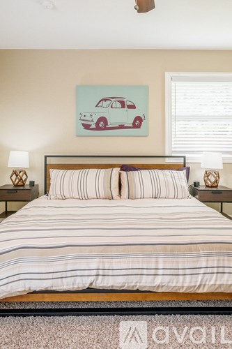 A bedroom with a bed, pillows, a ceiling fan, and a painting of a car on the wall.