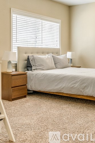 A bedroom with a bed, nightstand, and window with blinds.