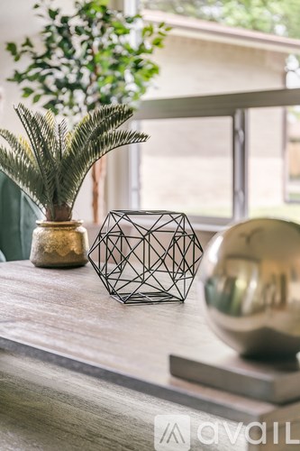 A table with a plant, a geometric vase, and a shiny sphere on it.
