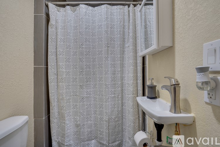 A bathroom with a white sink, toilet paper, and a shower curtain.
