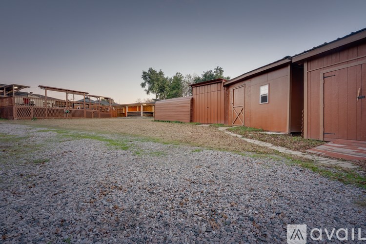 A gravel area with a building and a shed in the background.