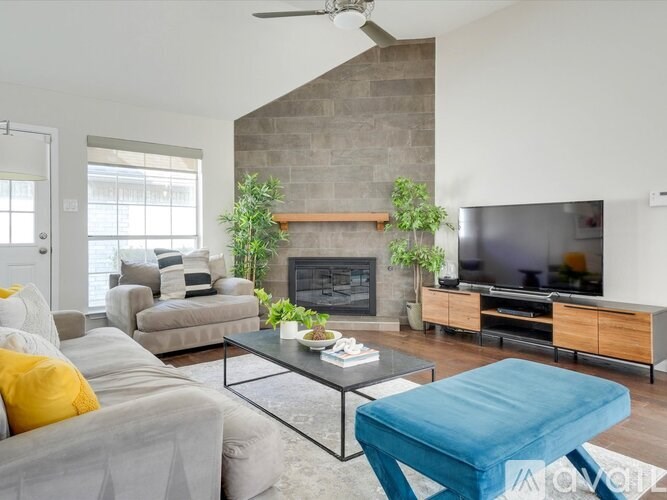A living room with a grey couch, a blue ottoman, a fireplace, and a television.