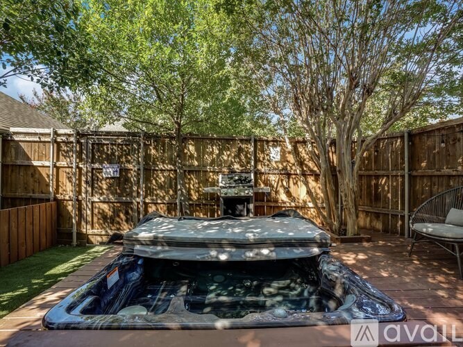 A hot tub is in the middle of a backyard with a wooden fence and trees.