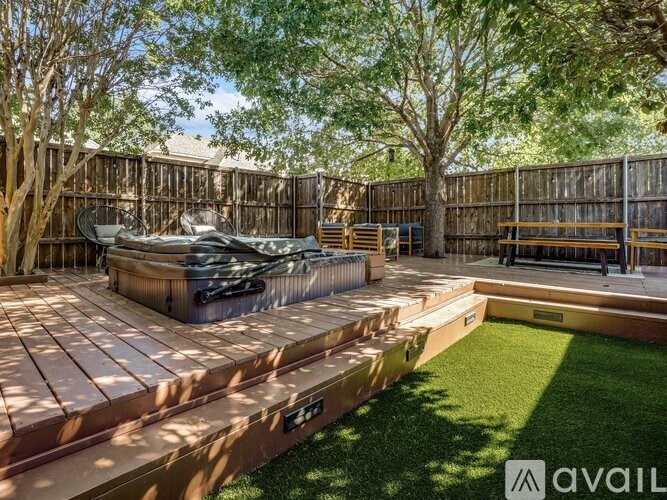 A backyard with a hot tub, wooden deck, and a fence.