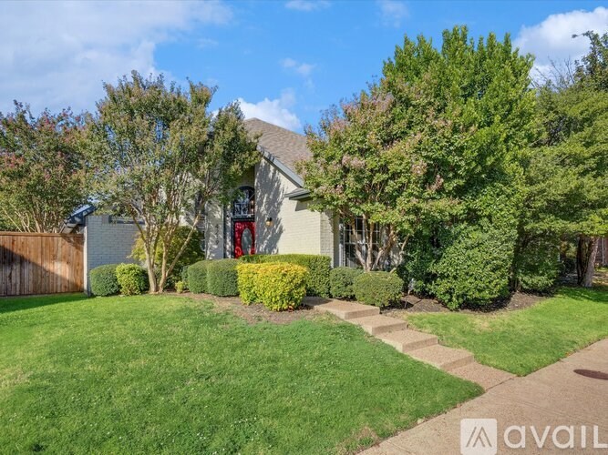 A house with a red door is surrounded by greenery and has a lawn in front.