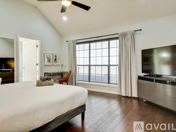 A bedroom with a large bed, a TV, and a window with curtains.