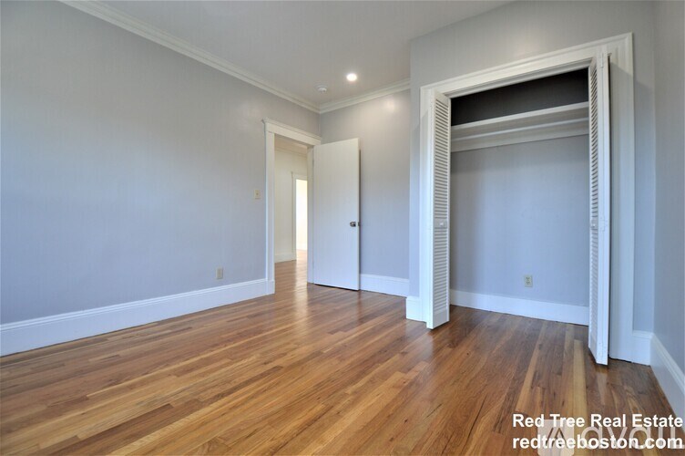 A room with wooden floors and white walls, with a doorway leading to another room.