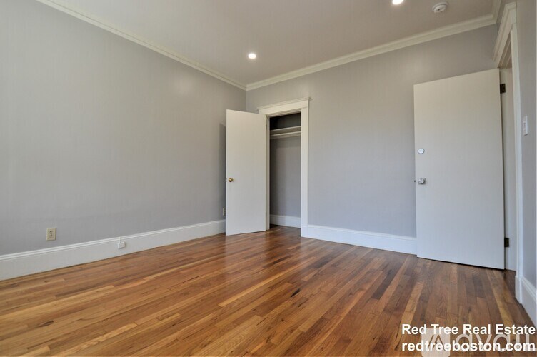 A room with wooden floors and white walls, with a doorway leading to another room.