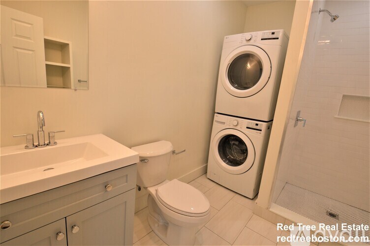 A white washer and dryer stand next to a toilet in a bathroom.