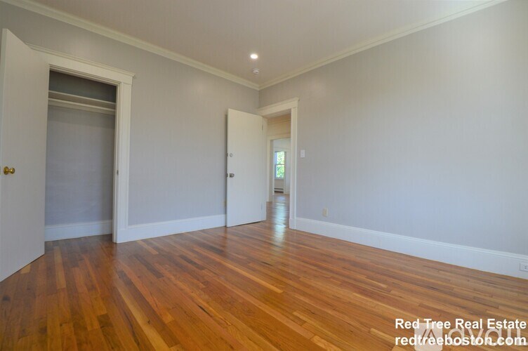 A room with wooden floors and white walls, with two doors and one window.