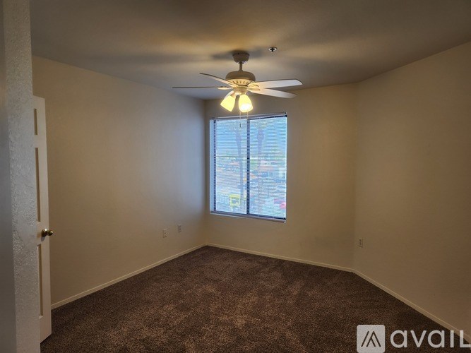 A room with a carpeted floor, a ceiling fan, and a window with blinds.