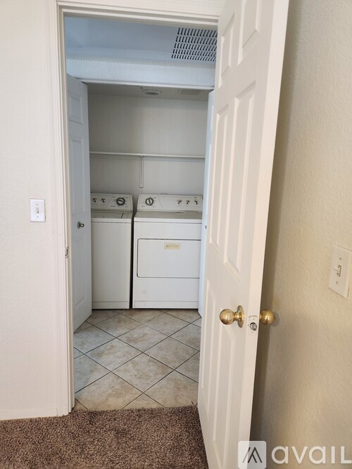A white door opens to a small kitchen with a dishwasher and a fridge.