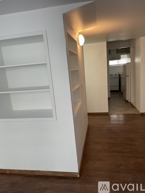 A long hallway with a light on the wall and a white shelf on the left.