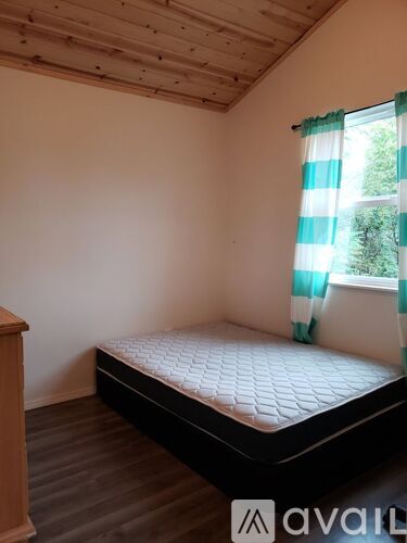 A bedroom with a bed, wooden floor, and a window with a green and white striped curtain.