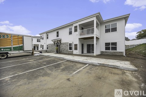 A white two-story building with a balcony on the second floor and a parking lot in front.