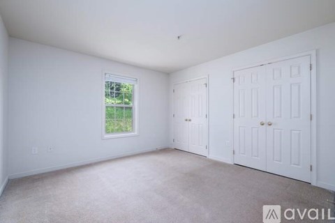A room with white walls and carpeted floor with two doors and a window.
