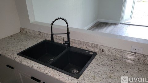 A kitchen sink with a black faucet on a granite countertop.