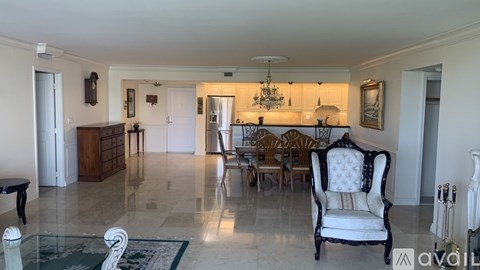 A living room with a white chair in the foreground and a dining area in the background.