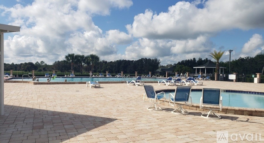 A sunny day at the pool with chairs and trees in the distance.