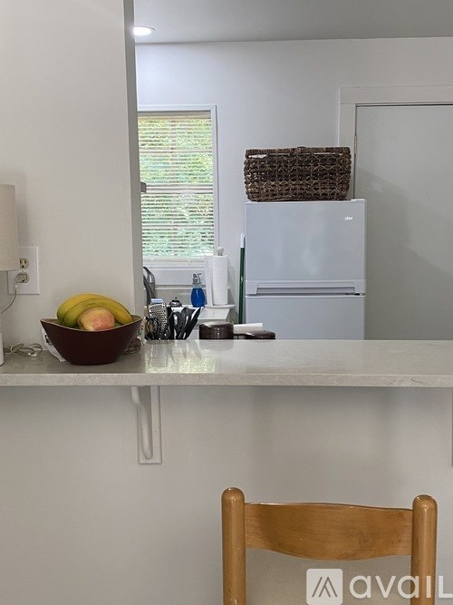 A kitchen with a white fridge, a bowl of fruit, and a wooden chair.