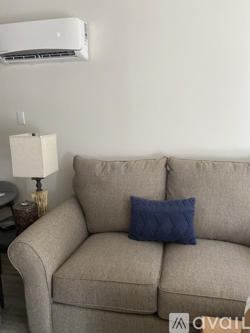 A beige couch with a blue pillow and a lamp on a side table.