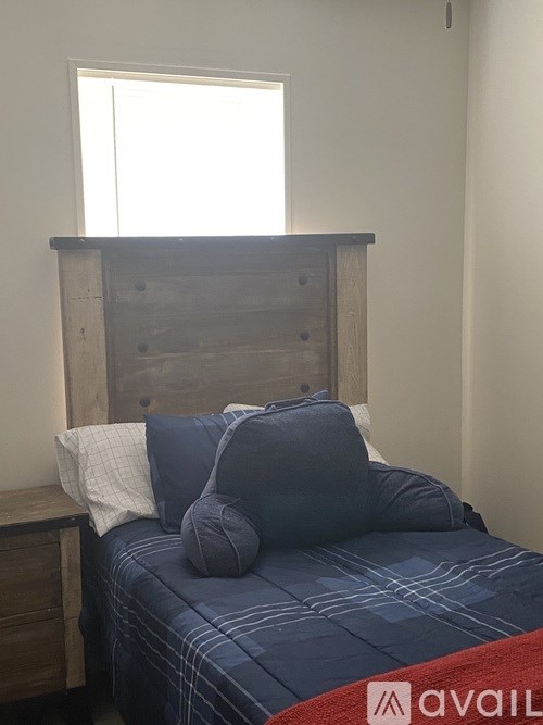 A bed with a wooden headboard and blue bedding with a window above it.