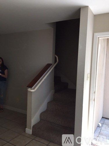 A woman stands in a hallway with a staircase.