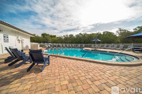 A pool surrounded by a brick patio and lounge chairs.