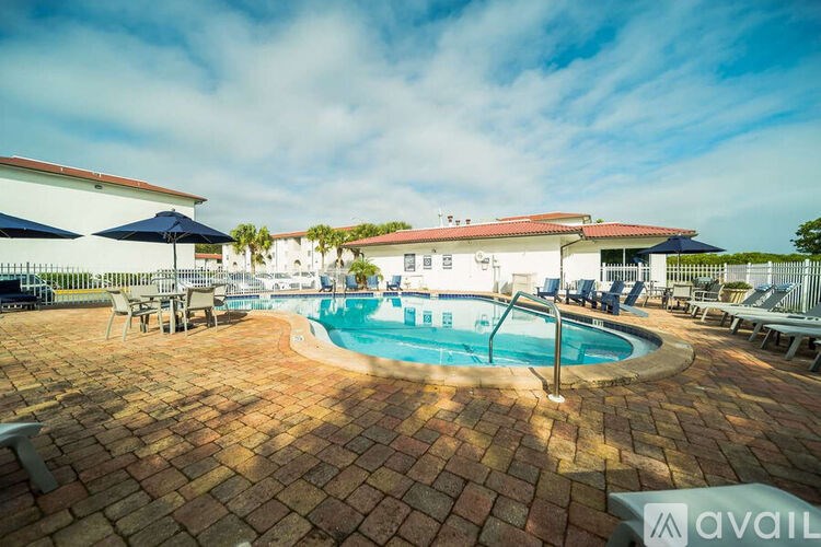 A pool surrounded by a brick patio with chairs and umbrellas.