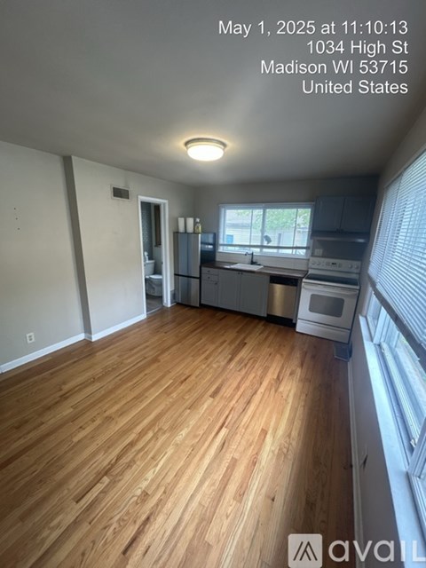 A kitchen with wooden flooring and a window with blinds.