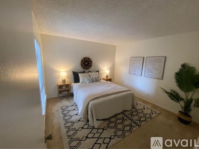 A bedroom with a large bed, a plant, and pictures on the wall.