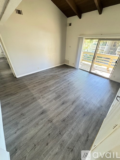 A room with wooden flooring and a sliding glass door leading to a balcony.