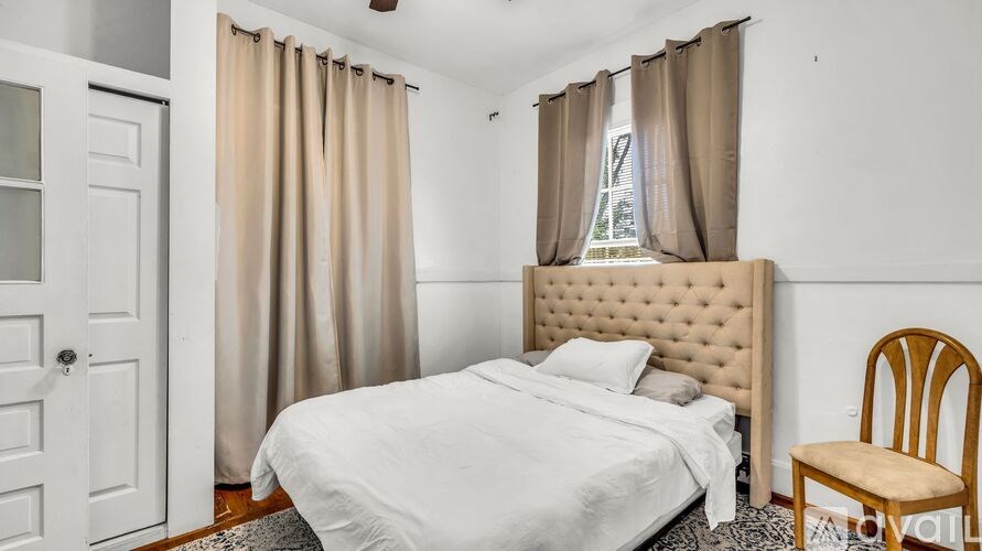 A bedroom with a white bed and a wooden chair.