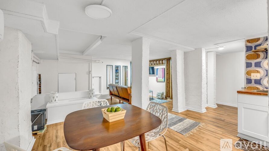A dining table with a bowl of fruit on it sits in the middle of a room with white walls and wooden floors.