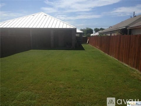 A backyard with a wooden fence and a white building in the background.