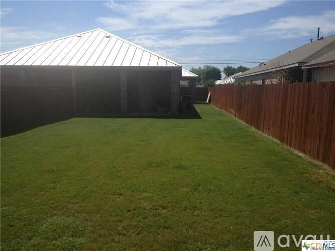 A backyard with a wooden fence and a white building in the background.