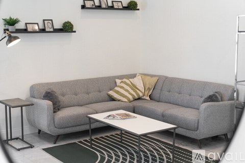A grey couch with a striped pillow and a white table in front of it.