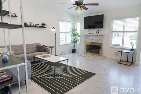 A living room with a grey couch, a black and white coffee table, a fireplace, and a flat screen TV mounted above it.