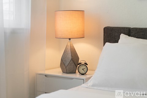 A bedside table with a lamp, clock, and pillow.
