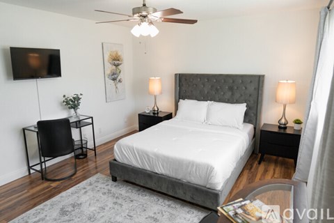A bedroom with a large bed, a ceiling fan, and a television mounted on the wall.